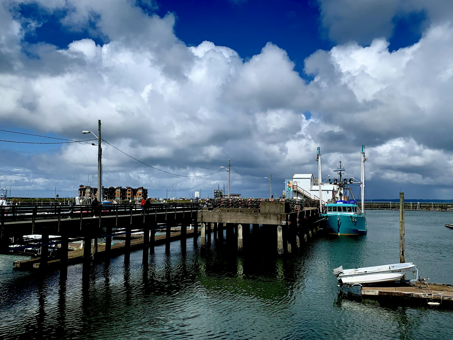 Small-harbour pier with moored fishing boat under big coastal clouds (placeholder photo)